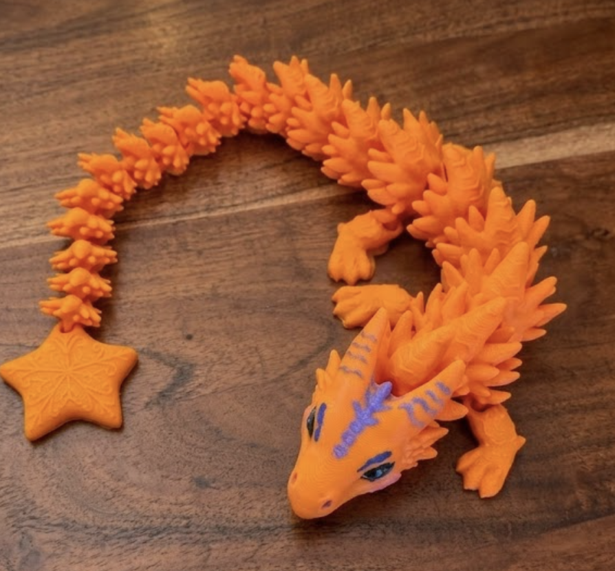 Detailaufnahme eines 3D-gedruckten Gelenkdrachen in Orange mit handbemalten blauen Akzenten und Stern-Anhänger